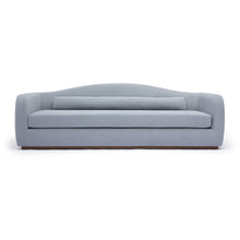 Load image into Gallery viewer, A modern three-seater sofa upholstered in a light blue-gray fabric, featuring a curved backrest, a matching lumbar pillow, and a low wooden base, shown against a plain white background.